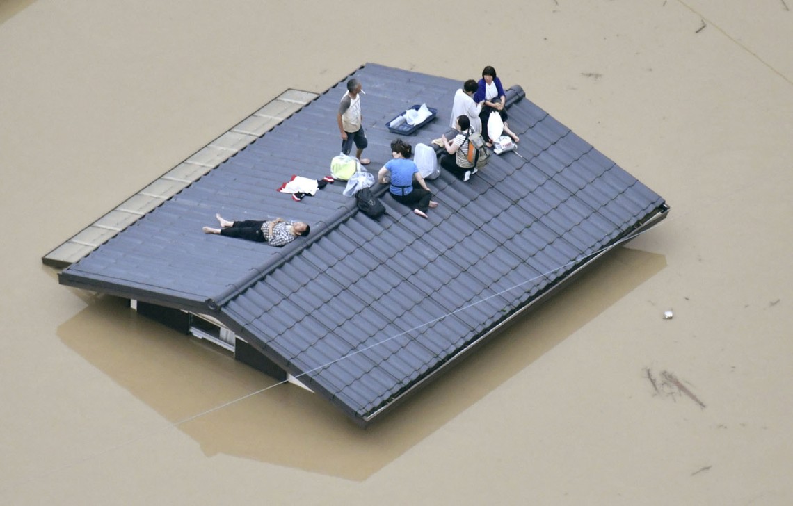 An aerial view shows local residents seen on the roof of submerged house at a flooded area as they wait for a rescue in Kurashiki